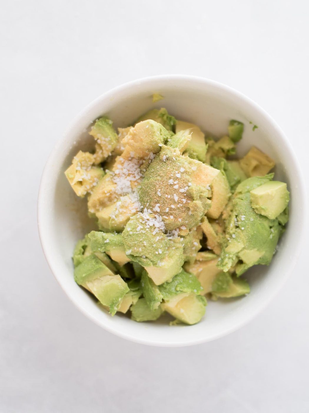 Chopped up pieces of avocado in a bowl with garlic powder and salt over it.