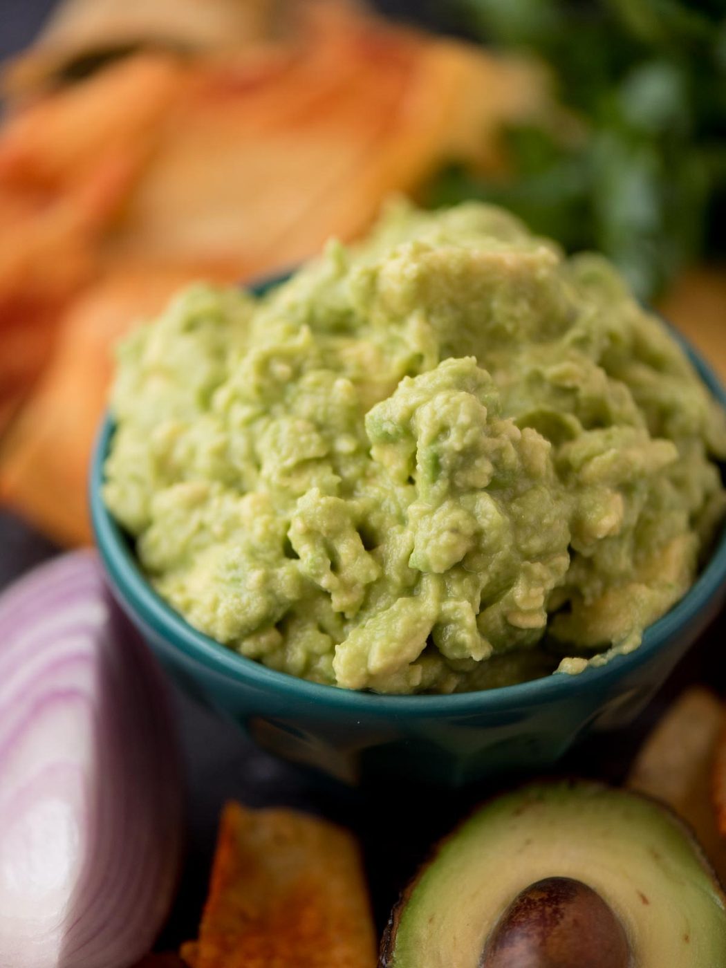 Small bowl of 4 ingredient guacamole with half an avocado and red onion next to it.
