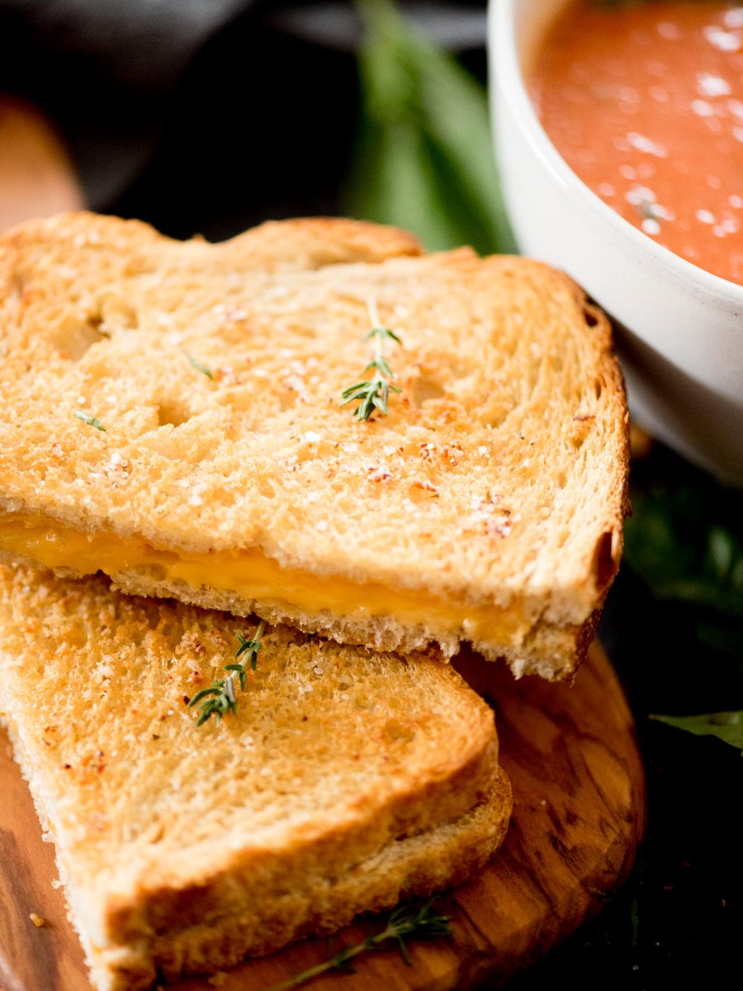 air fried grilled cheese sandwich cut in half next to a bowl of tomato basil soup and topped with a small sprig of thyme