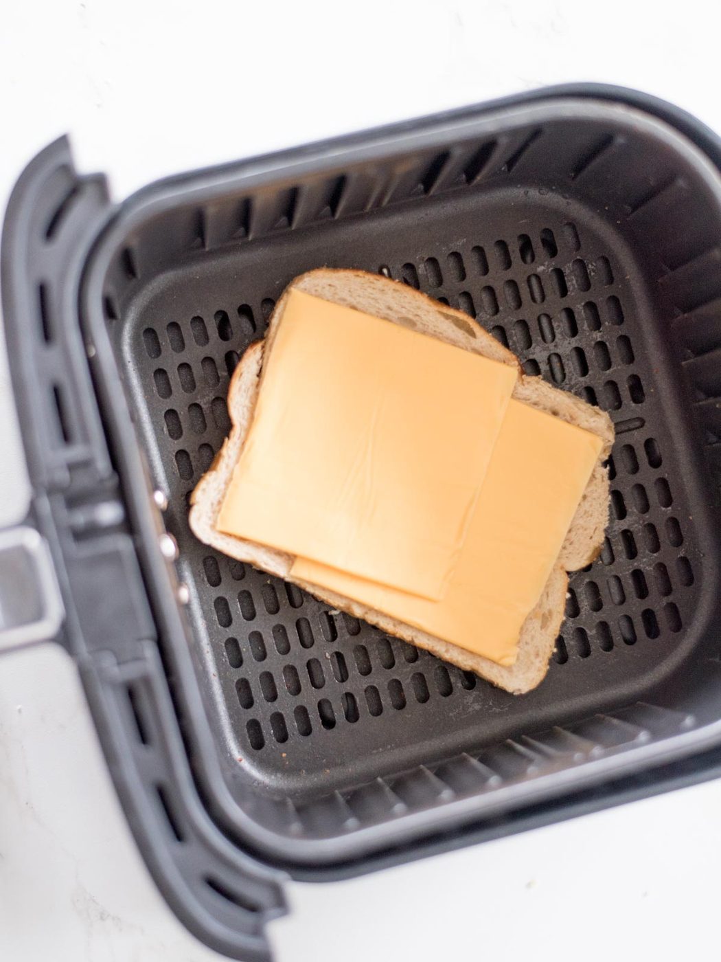 two slices of cheese on a piece of bread inside the air fryer basket