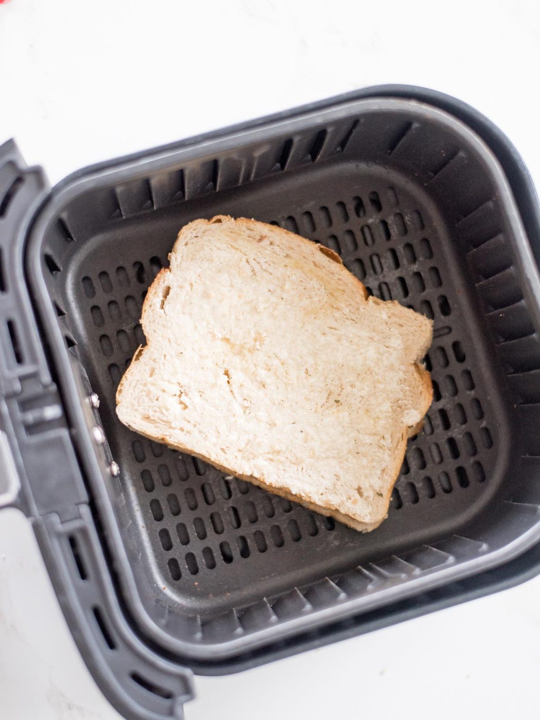 uncooked cheese sandwich with buttered bread sitting inside an air fryer basket