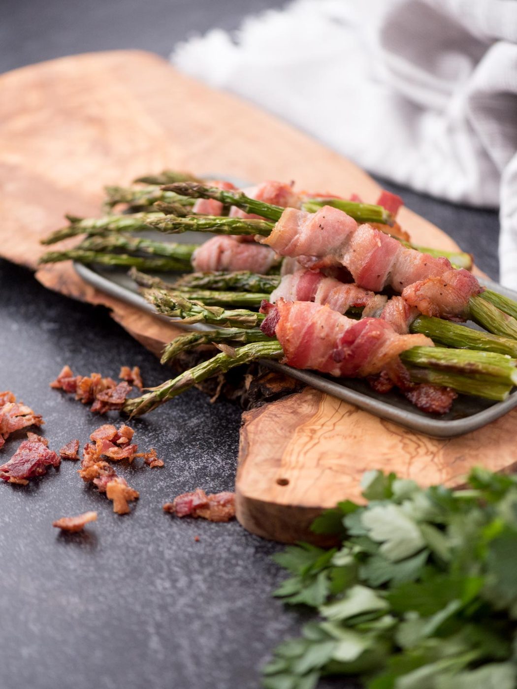 Platter of bacon wrapped asapargus with crispy bacon pieces around the edge.