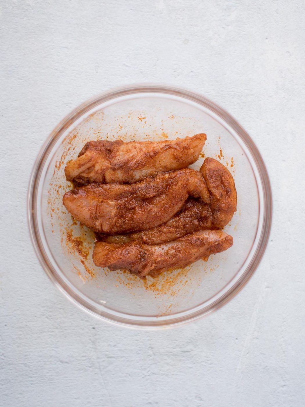 Seasoned chicken pieces, ready to transform into crispy air fryer chicken tenders, sit invitingly in a clear glass bowl on a light gray surface.