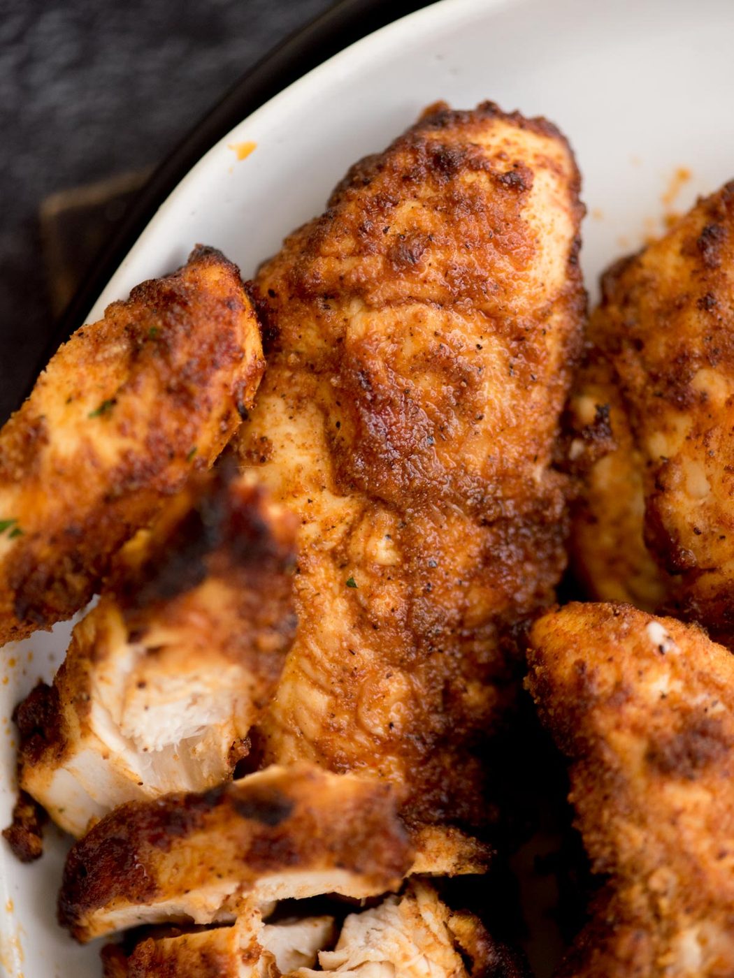 Close-up of a plate with crispy, golden-brown air fryer chicken tenders. The chicken is seasoned, boasting a textured, crunchy coating that catches the eye. Set against a dark background, these tenders shine with an appetizing color that teases the taste buds.