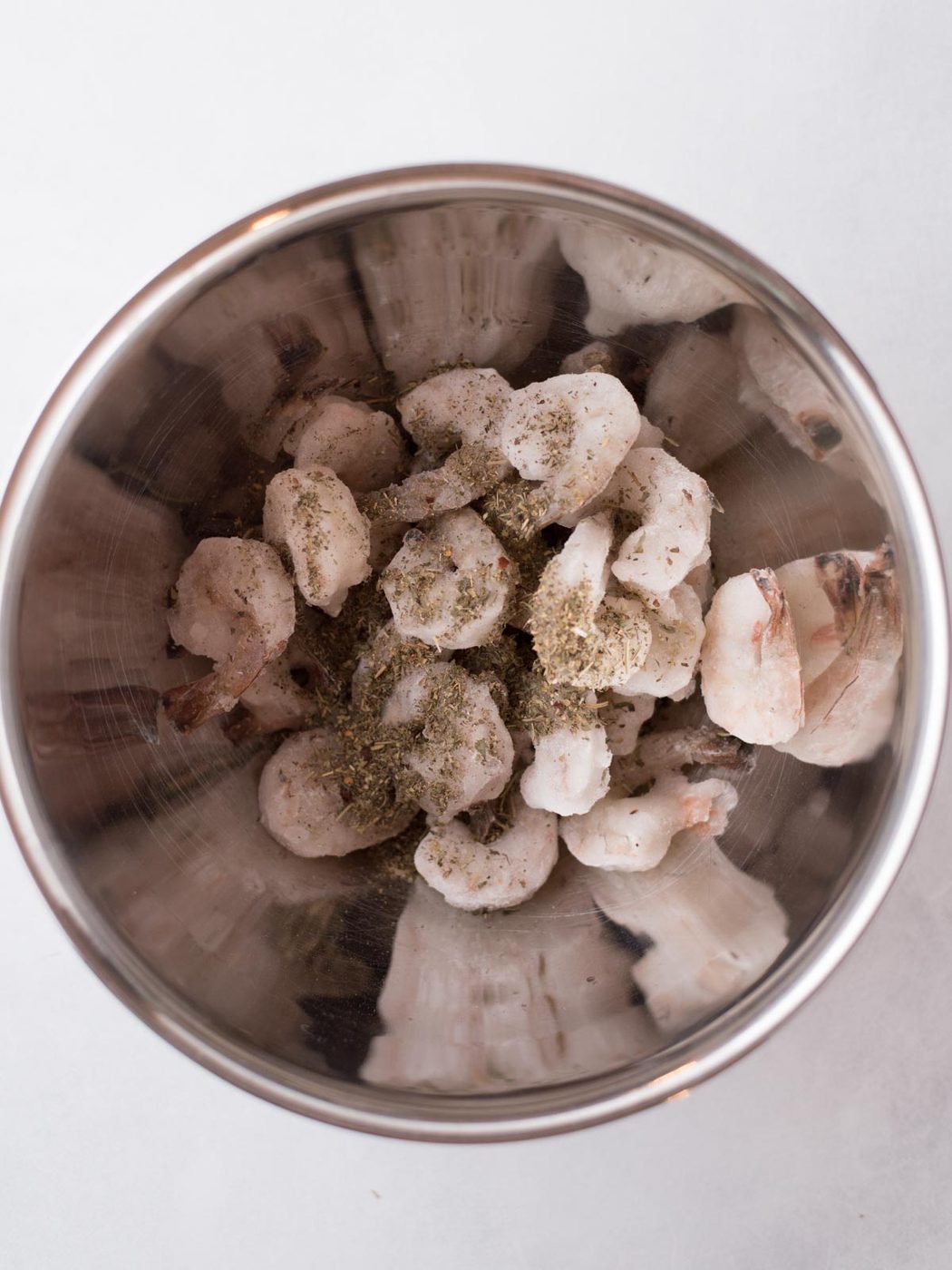 Seasoning tossed into a bowl of frozen shrimp in a mixing bowl.