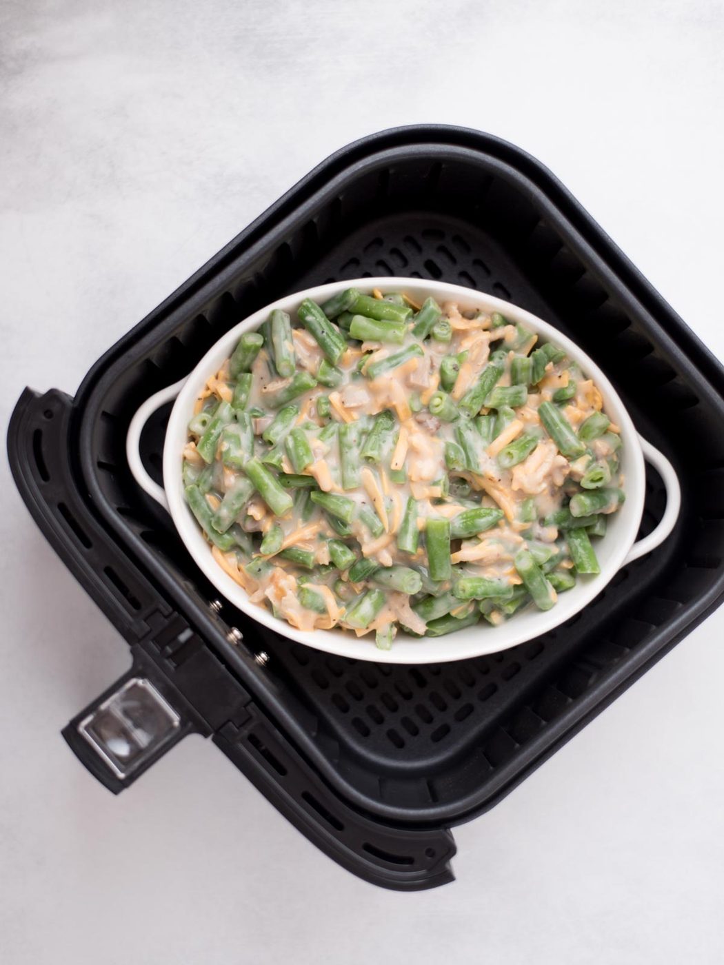 Baking dish in the air fryer filled with green bean casserole ready to cook.