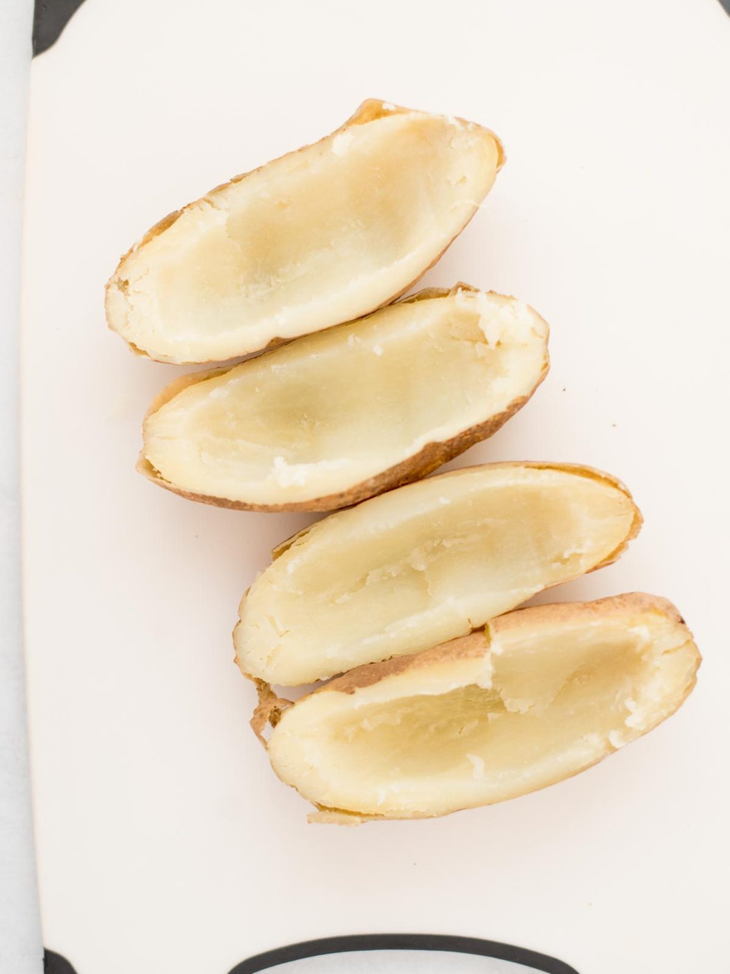 4 russet potatoes hallowed out and ready to prepare laying on parchment paper.