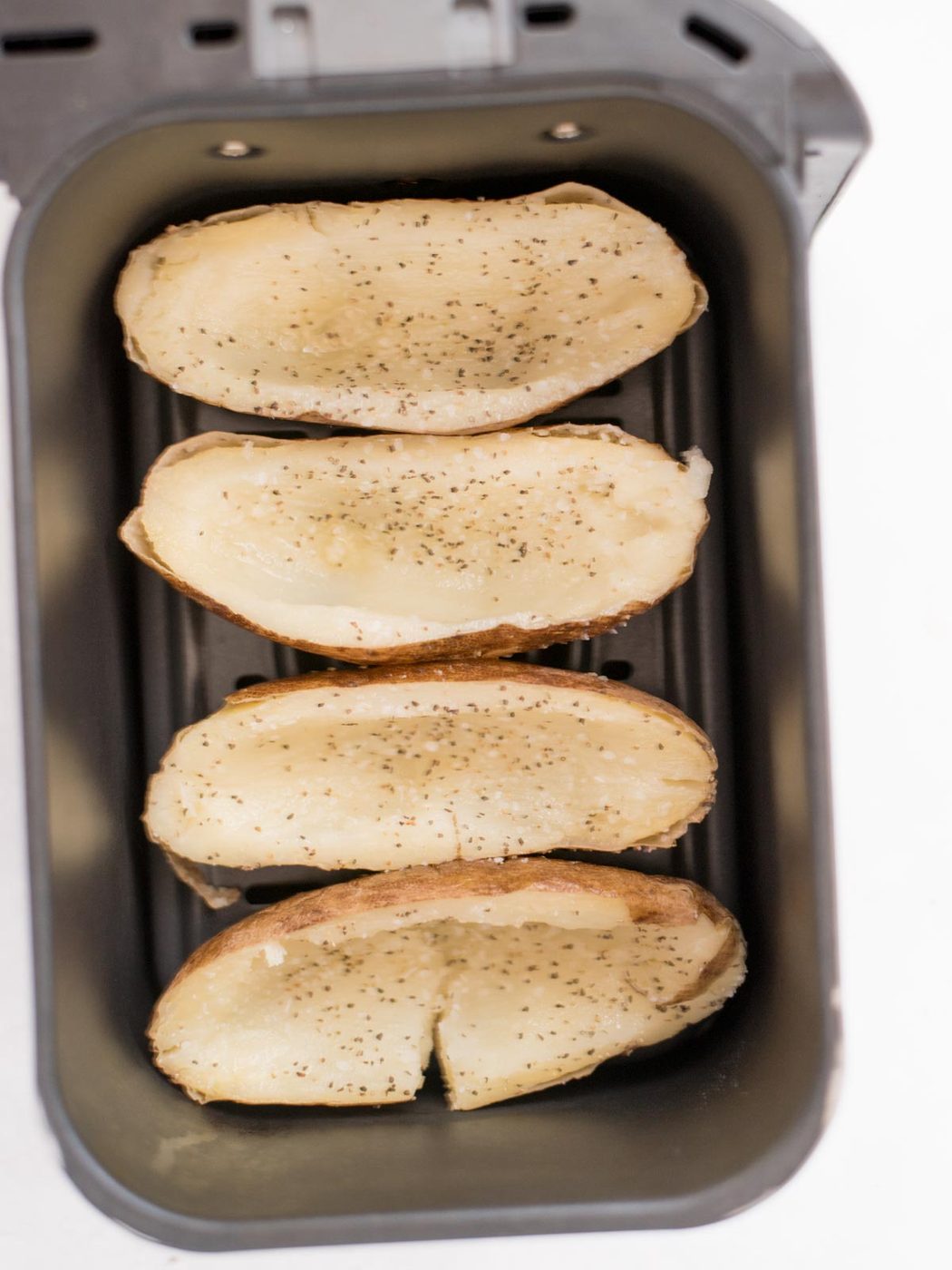 4 hallowed out potato halves added to an air fryer bucket that have been sprinkled with salt & pepper.