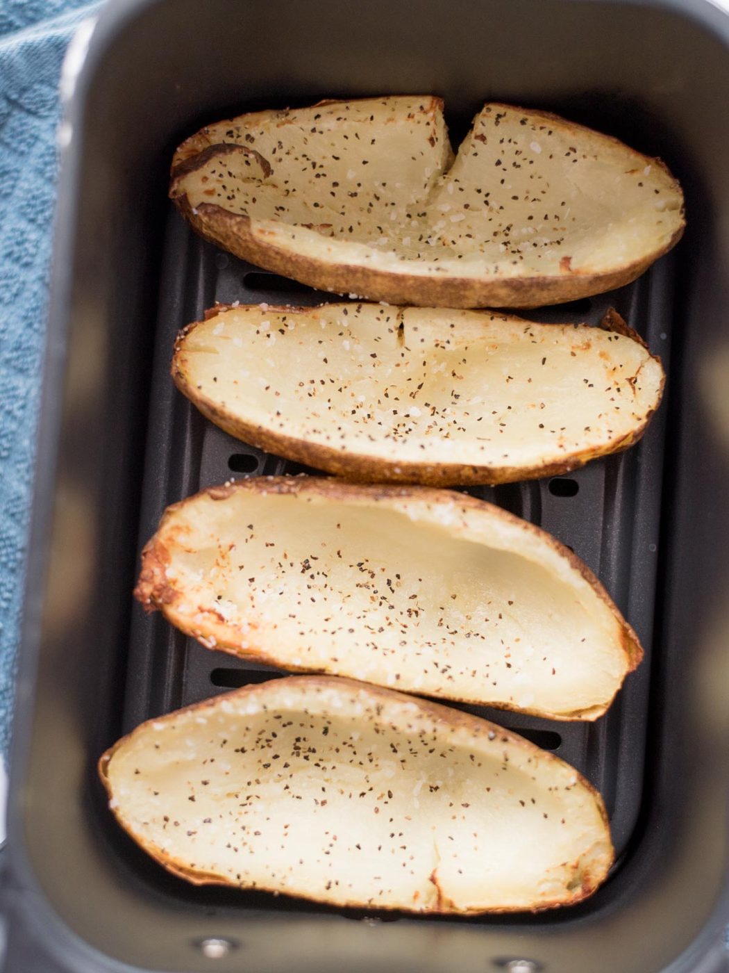 4 russet potatos with the potato scooped out of the middle and seasoned with salt and pepper laying inside an air fryer bucket.