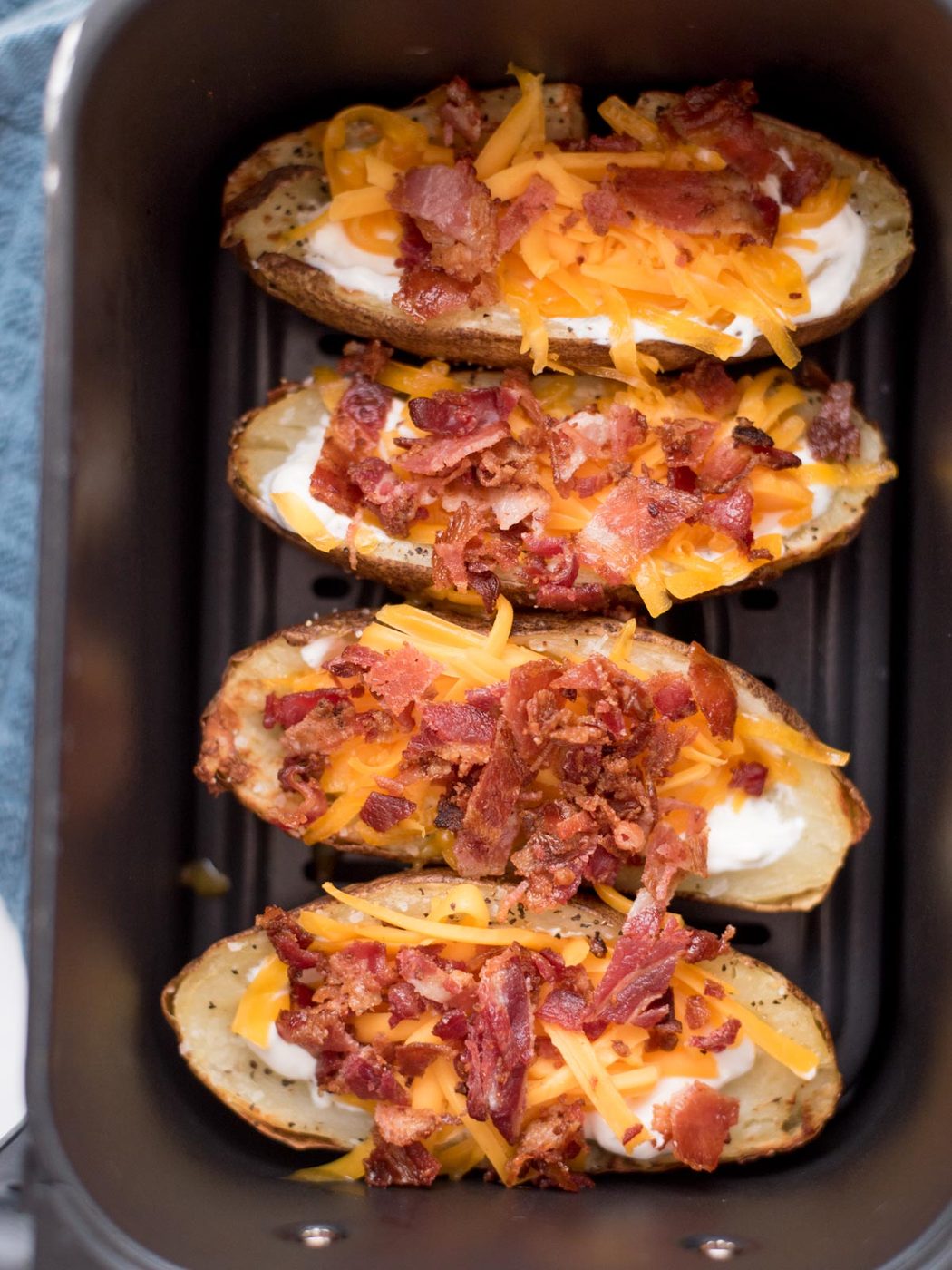 4 potato halves inside an air fryer bucket with sour cream, cheese and bacon loaded into them.