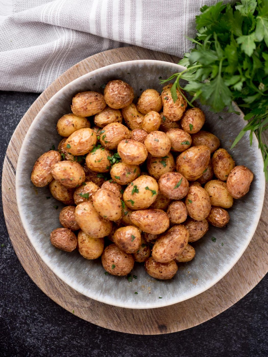 air fried baby potatoes in a bowl topped with fresh parsley. The potatoes are in a bowl surrounded by fresh parsley and a kitchen towel.