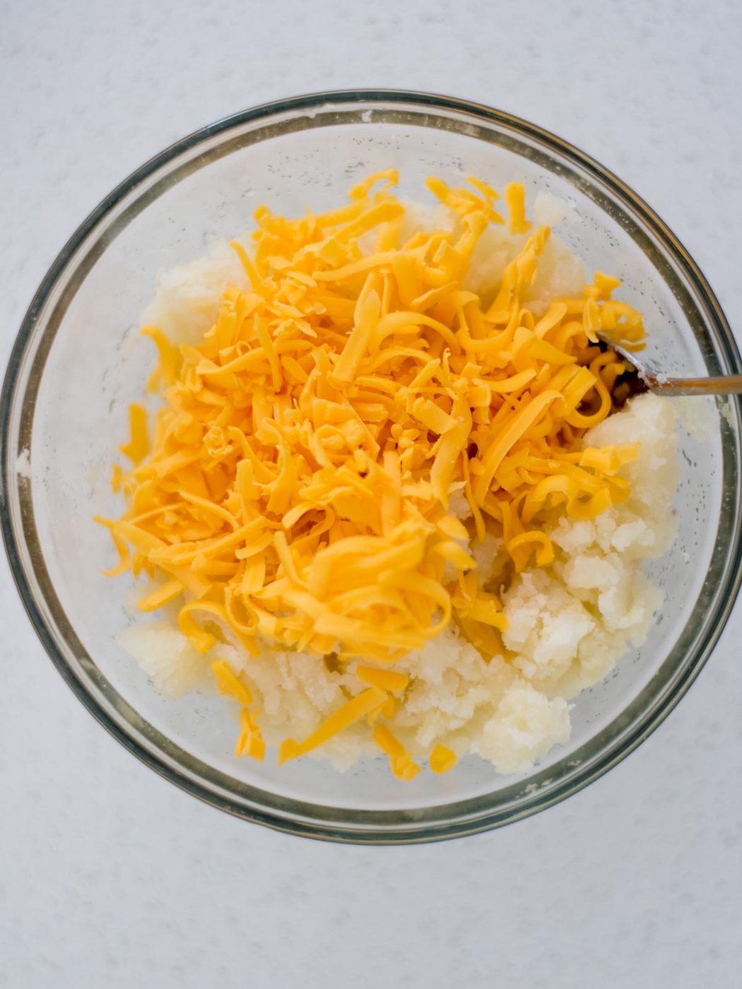 Potatoes and shredded cheese added to a mixing bowl for twice baked potatoes.