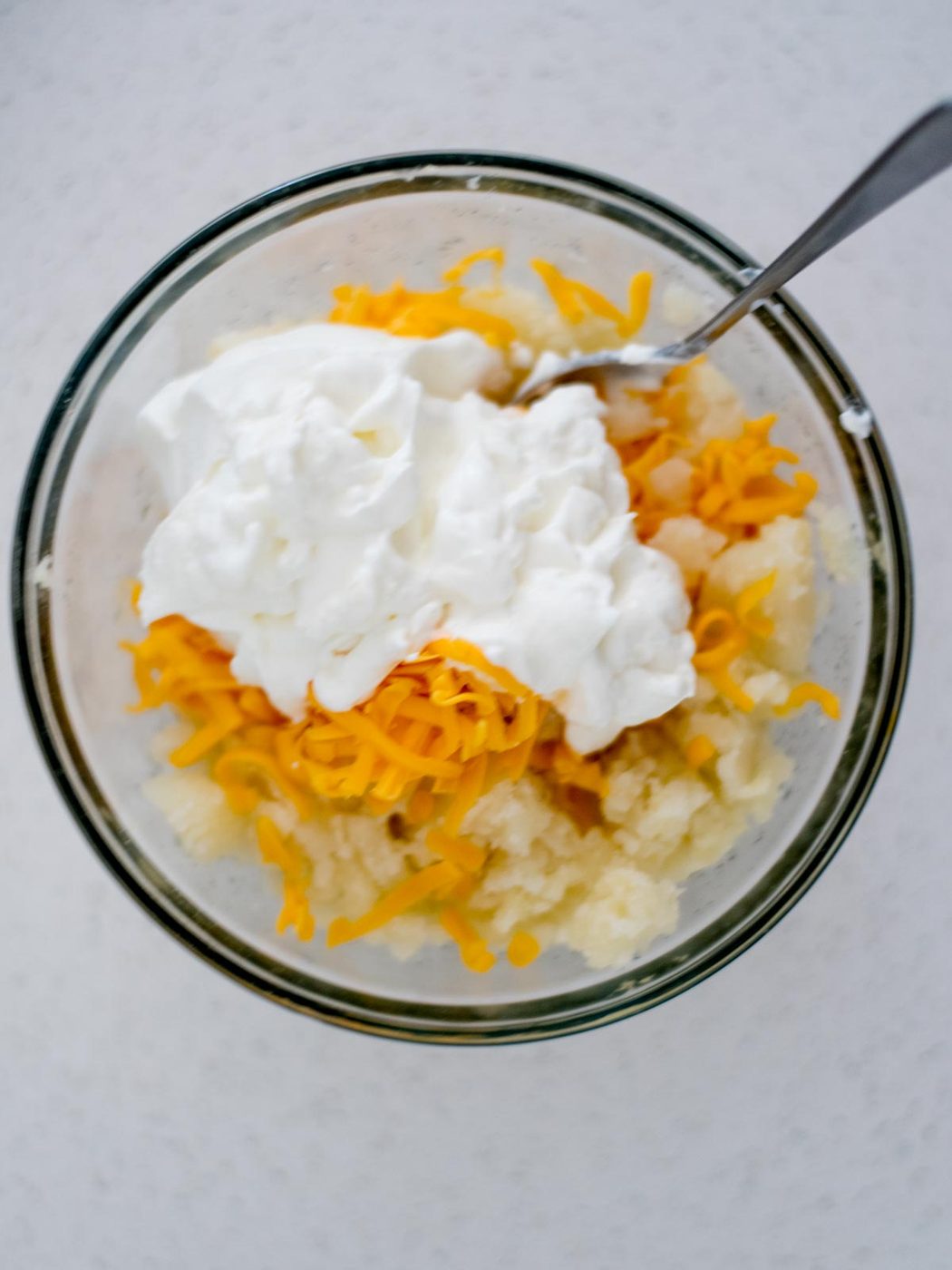 Potatoes, shredded cheese and sour cream added to a mixing bowl for twice baked potatoes.