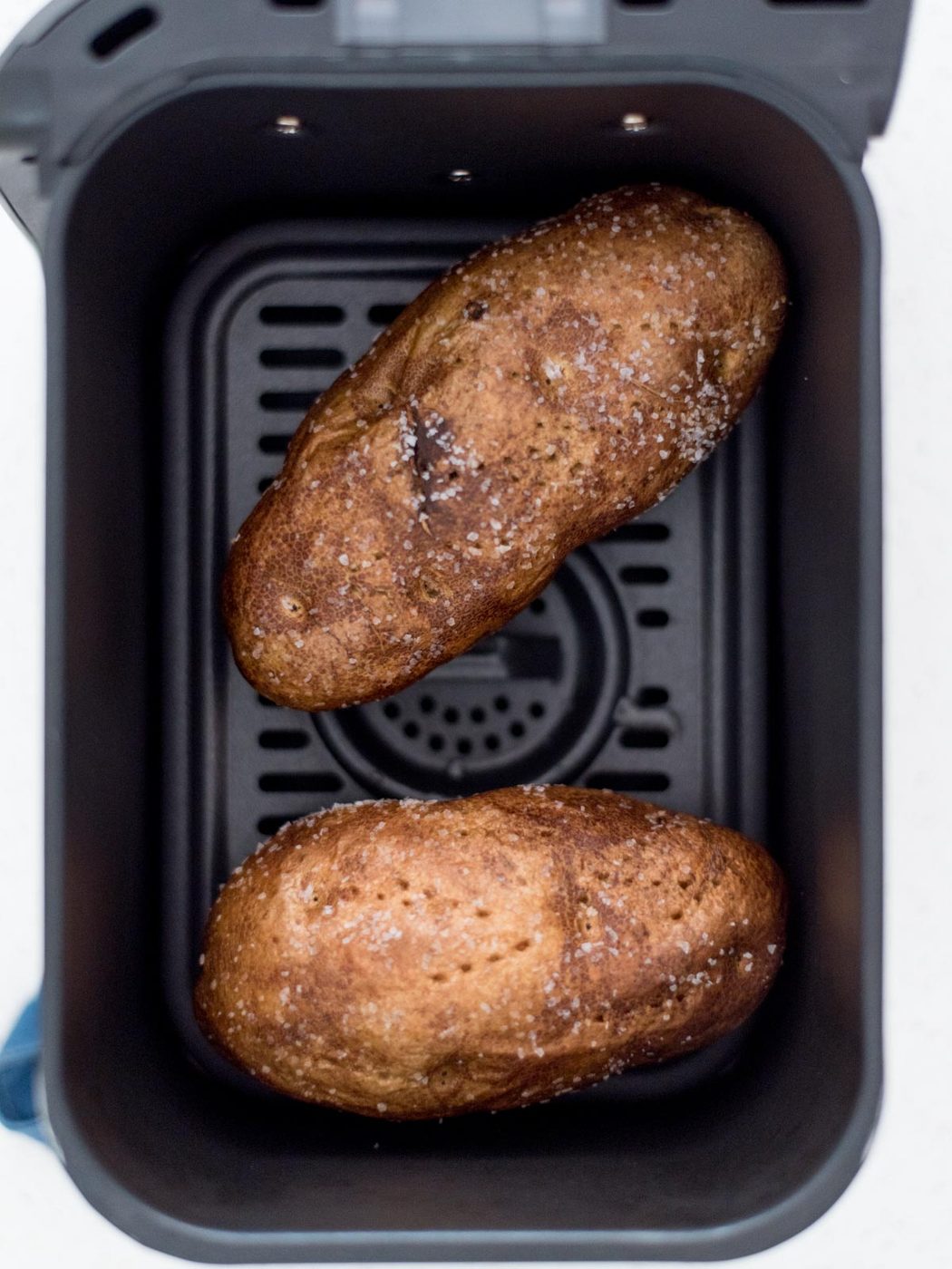 Two potatoes with salt and oil rubbed on them in an air fryer.