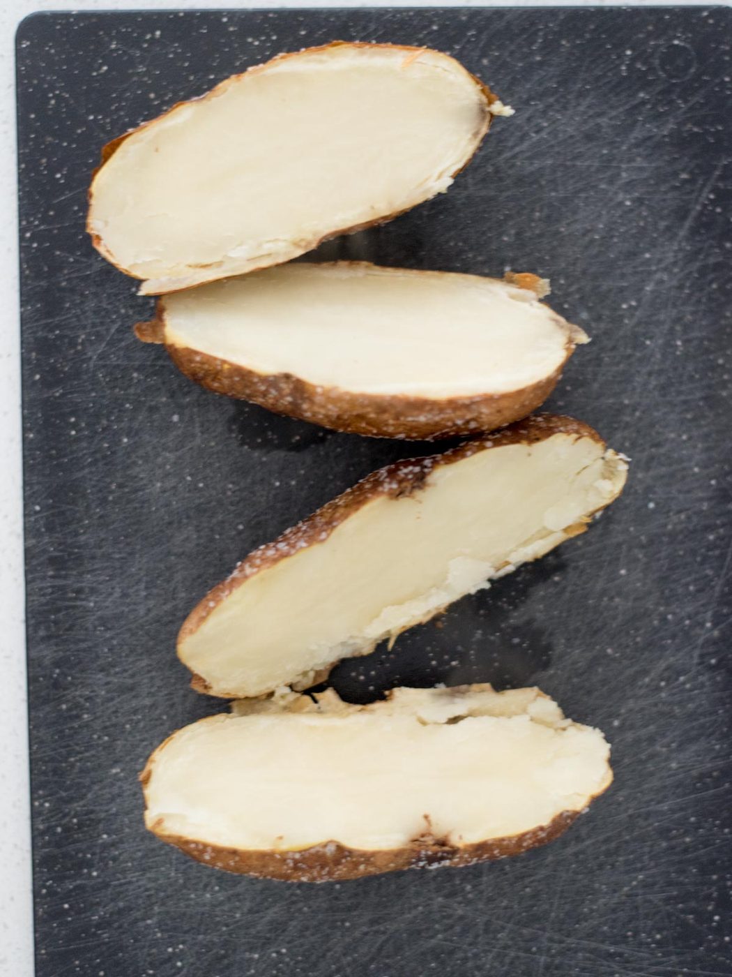 Cooked potatoes cut in half on a cutting board.