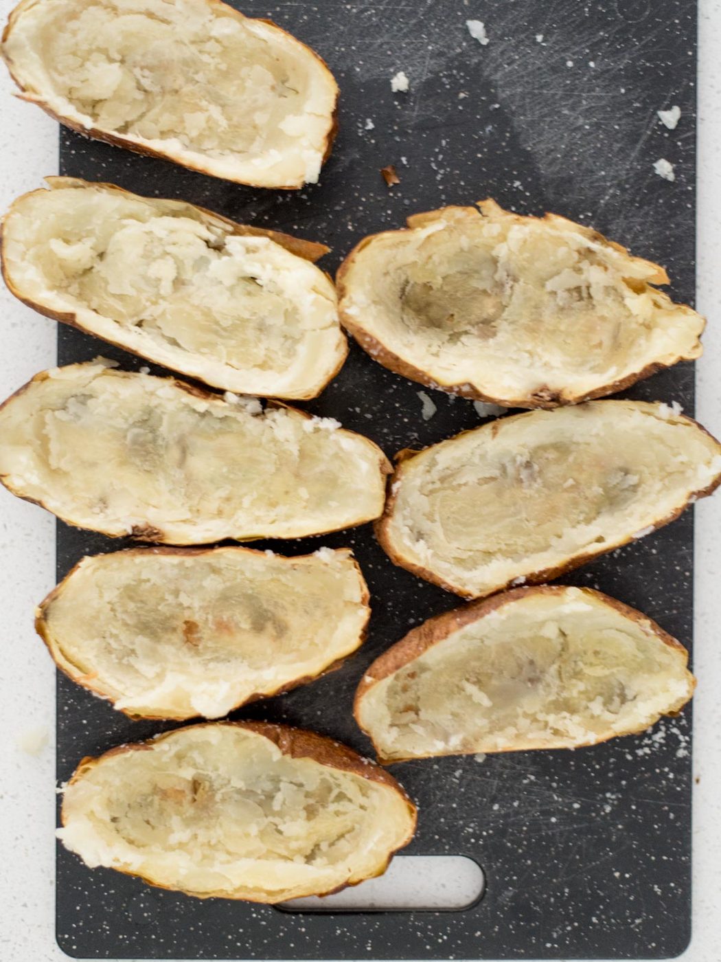 Potato skins on a cutting board with the potatos removed from the middle.