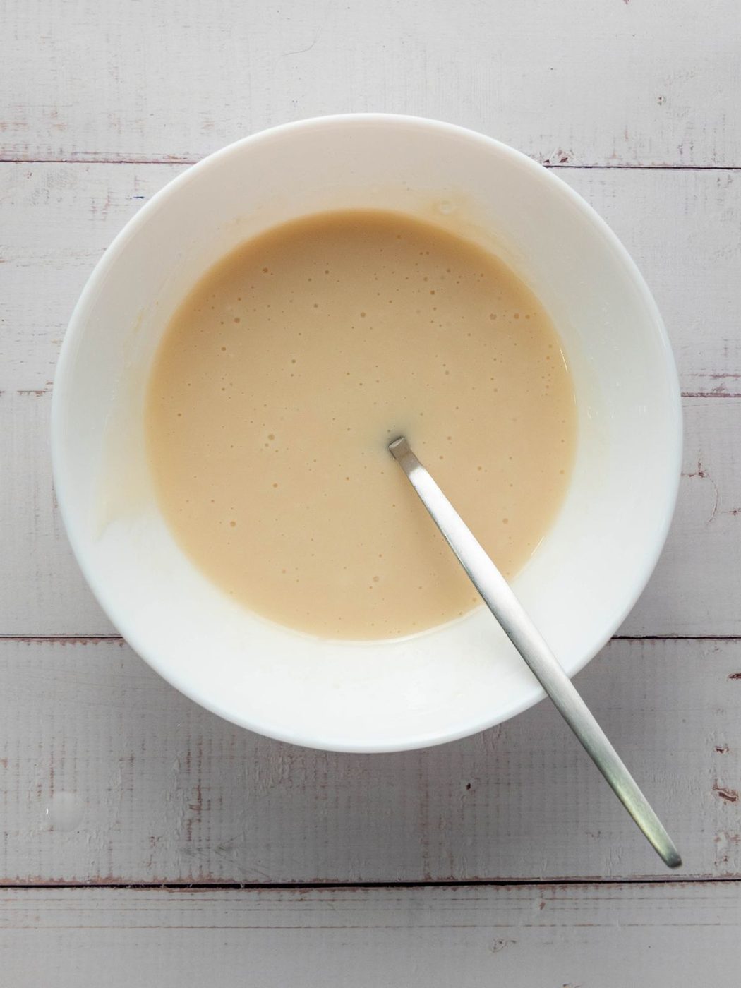 A white bowl filled with light-colored cake batter and a metal spoon.