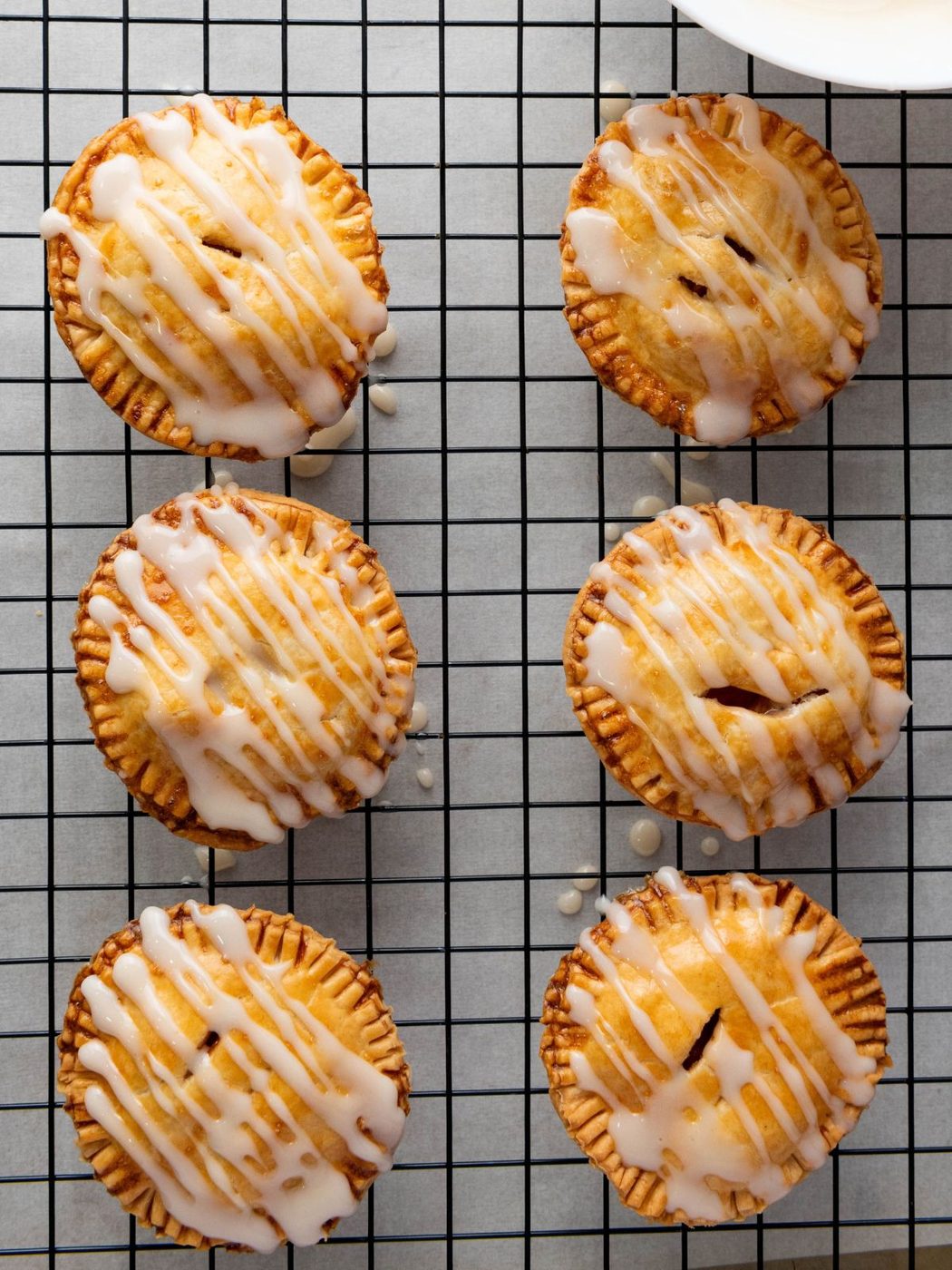 Six golden-brown mini pies with white icing drizzled over the top, resting on a wire cooling rack.