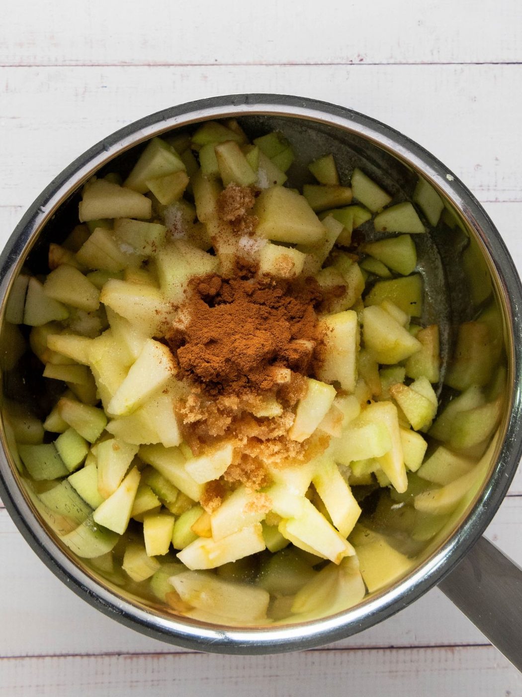 A metal pot filled with chopped apples, topped with a mound of brown sugar and cinnamon.