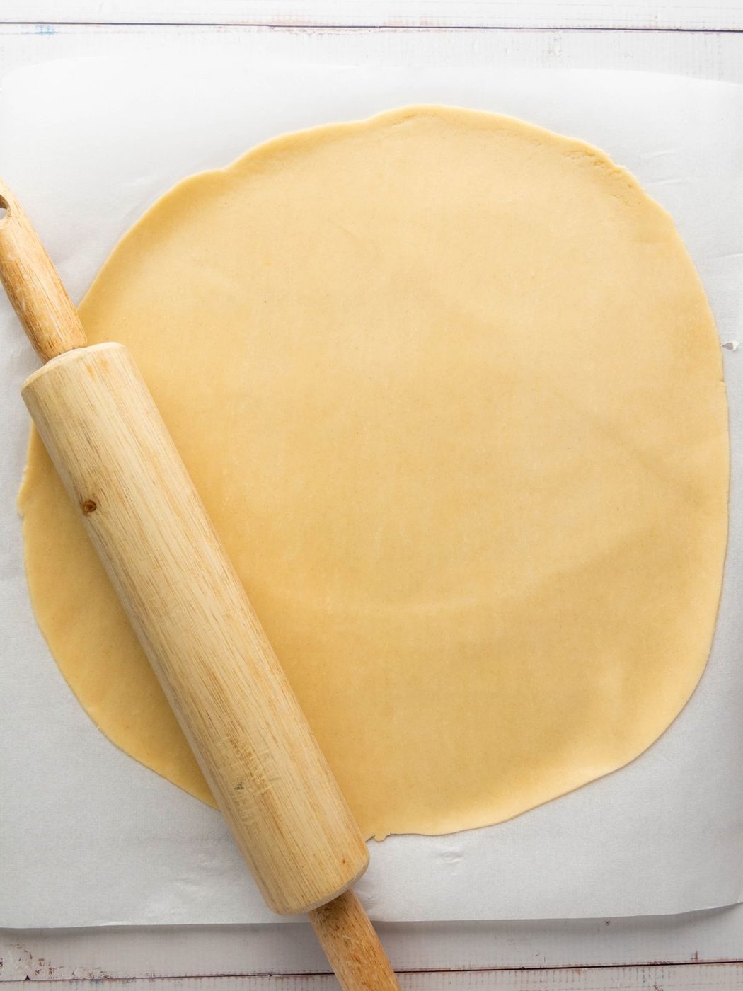 A wooden rolling pin resting on a sheet of rolled-out pie dough.