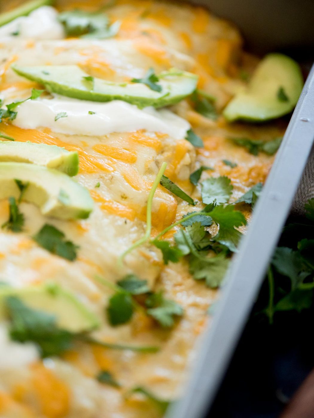 green chile chicken enchiladas topped with sour cream, cilantro, and avocado