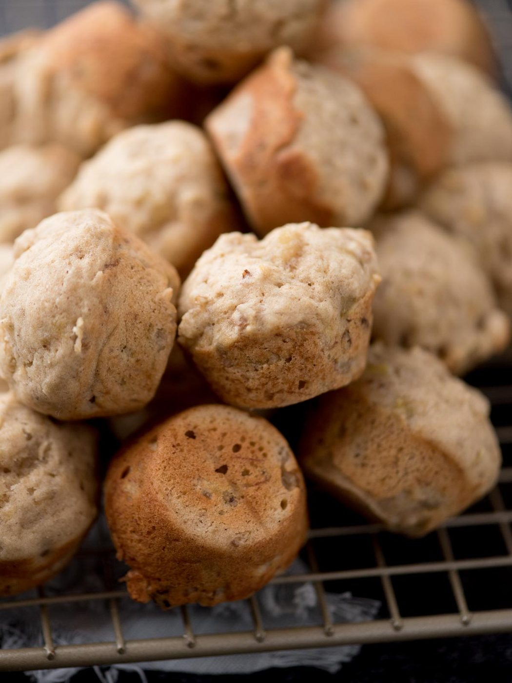 A close-up of freshly baked mini muffins with a light golden-brown color, stacked on a cooling rack.