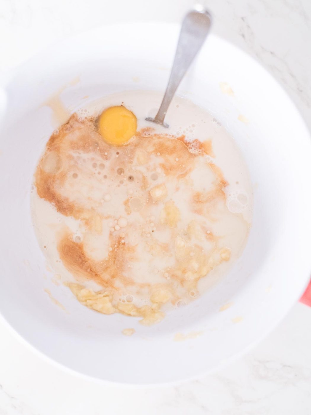 coconut oil added to the remaining wet ingredients for banana muffins in a mixing bowl