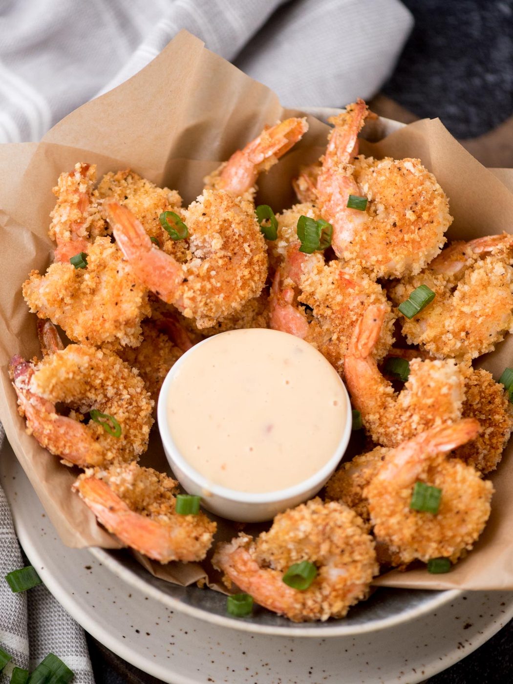bang bang shrimp in a bowl with sauce in a small white bowl. All of it is topped with sliced green onions.