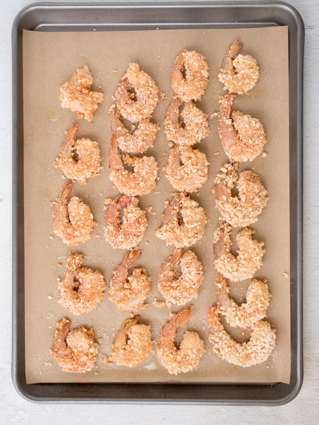 Breaded shrimp on a parchment lined baking sheet ready to bake.