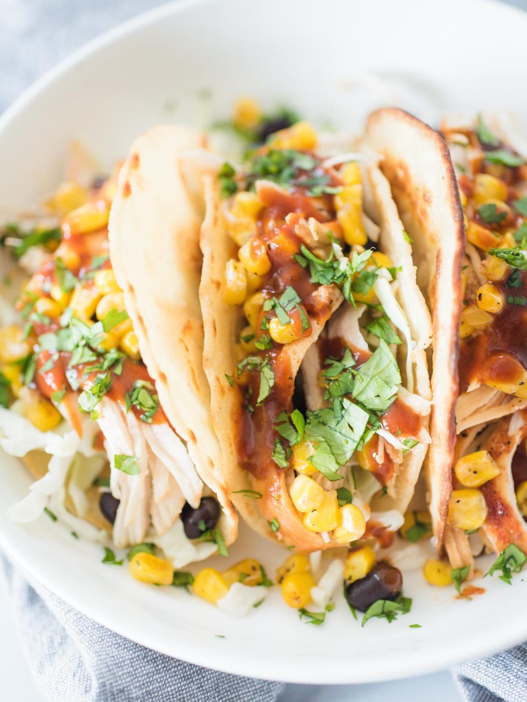 white plate with tacos standing up full of bbq chicken and toppings