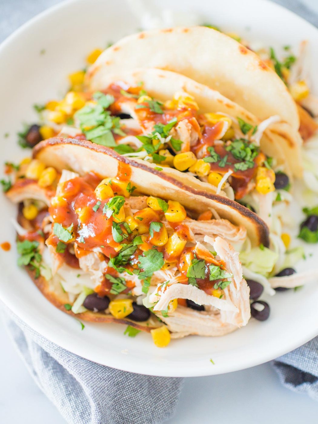 a shallow white bowl with chicken tacos stuffed with bbq chicken, beans, corn, and cilantro
