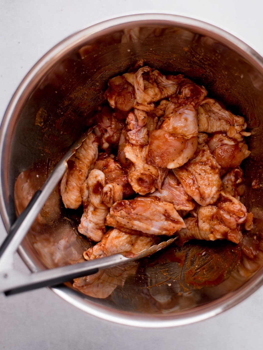 uncooked wings topped with seasoning and bbq sauce in a stainless steel mixing bowl