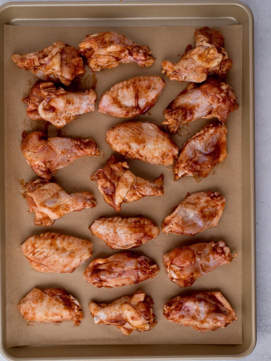 uncooked chicken wings coated in seasoning and bbq sauce on a parchment lined baking sheet