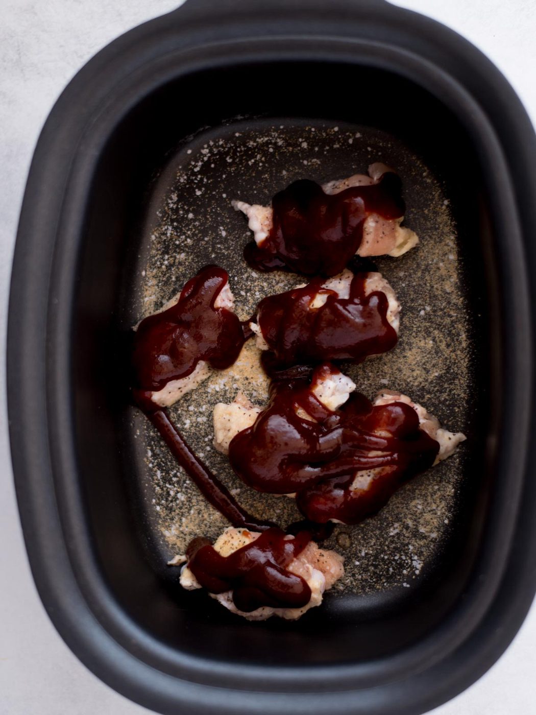 BBQ sauce poured over the seasoned raw chicken wings, ready to cook.