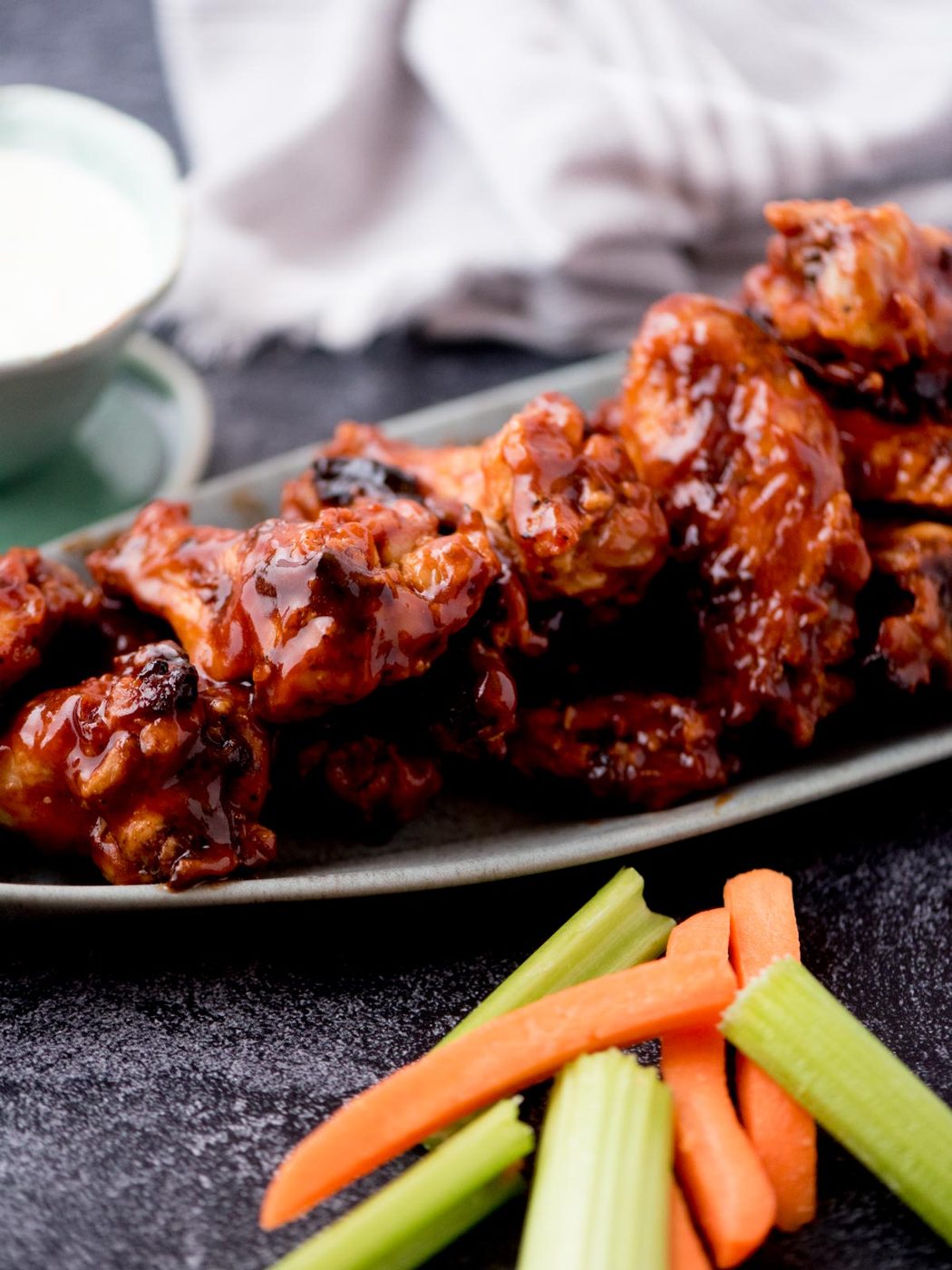 Carrots and celery laying next to a serving platter of bbq chicken wings.