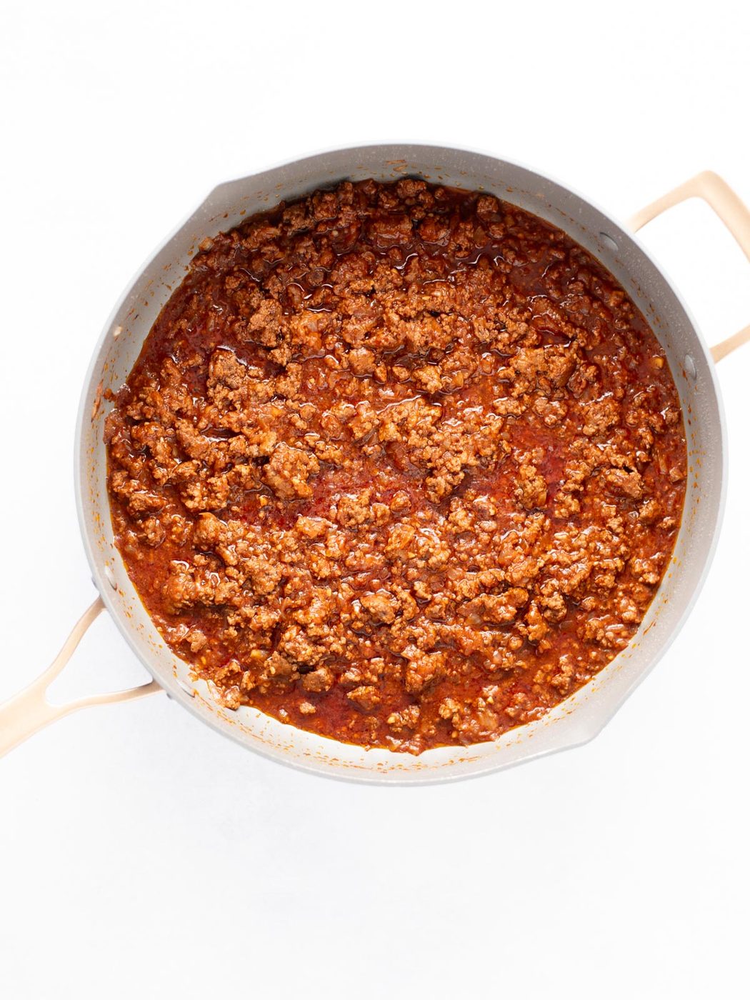 A large skillet filled with cooked ground beef in a rich red tomato sauce, viewed from above on a white background.