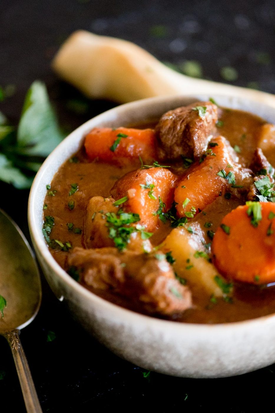 classic beef stew served in a bowl topped with parsley and breadsticks