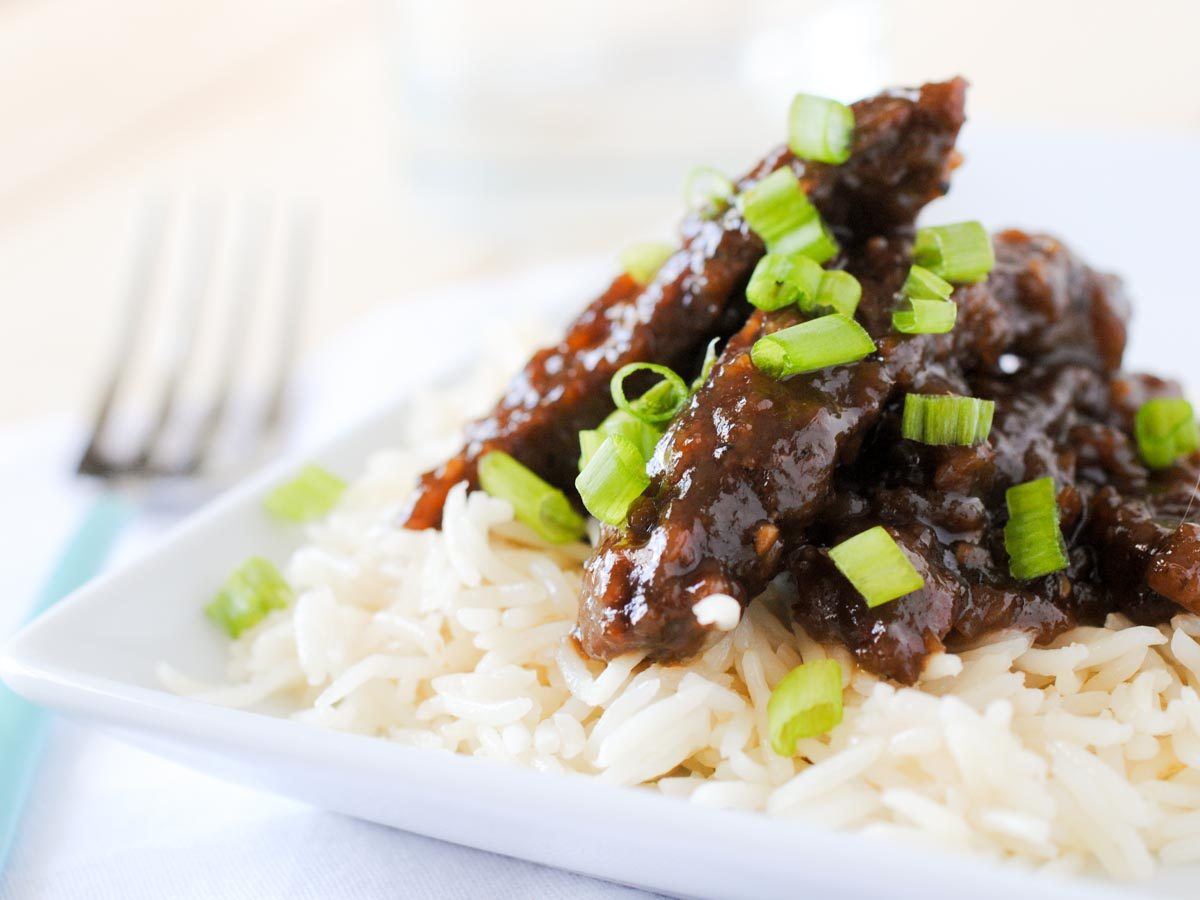 beef teriyaki on white rice topped with green onions on a white plate