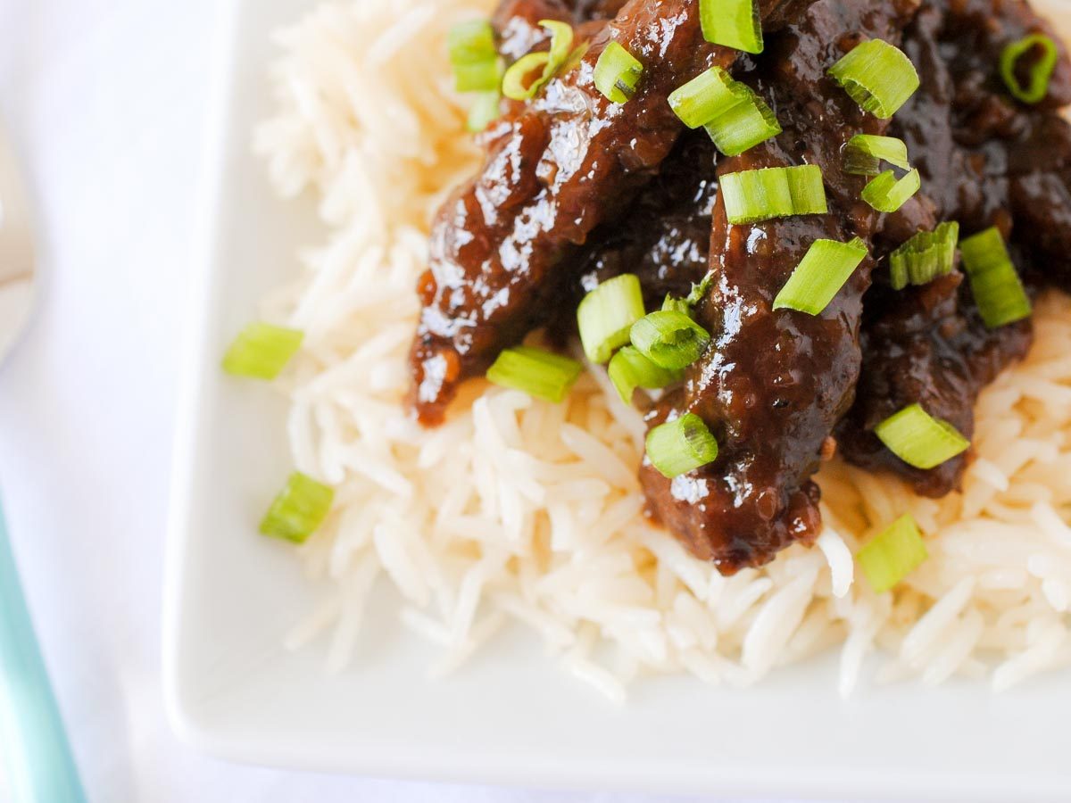 beef teriyaki on a plate of white rice topped with sliced green onions