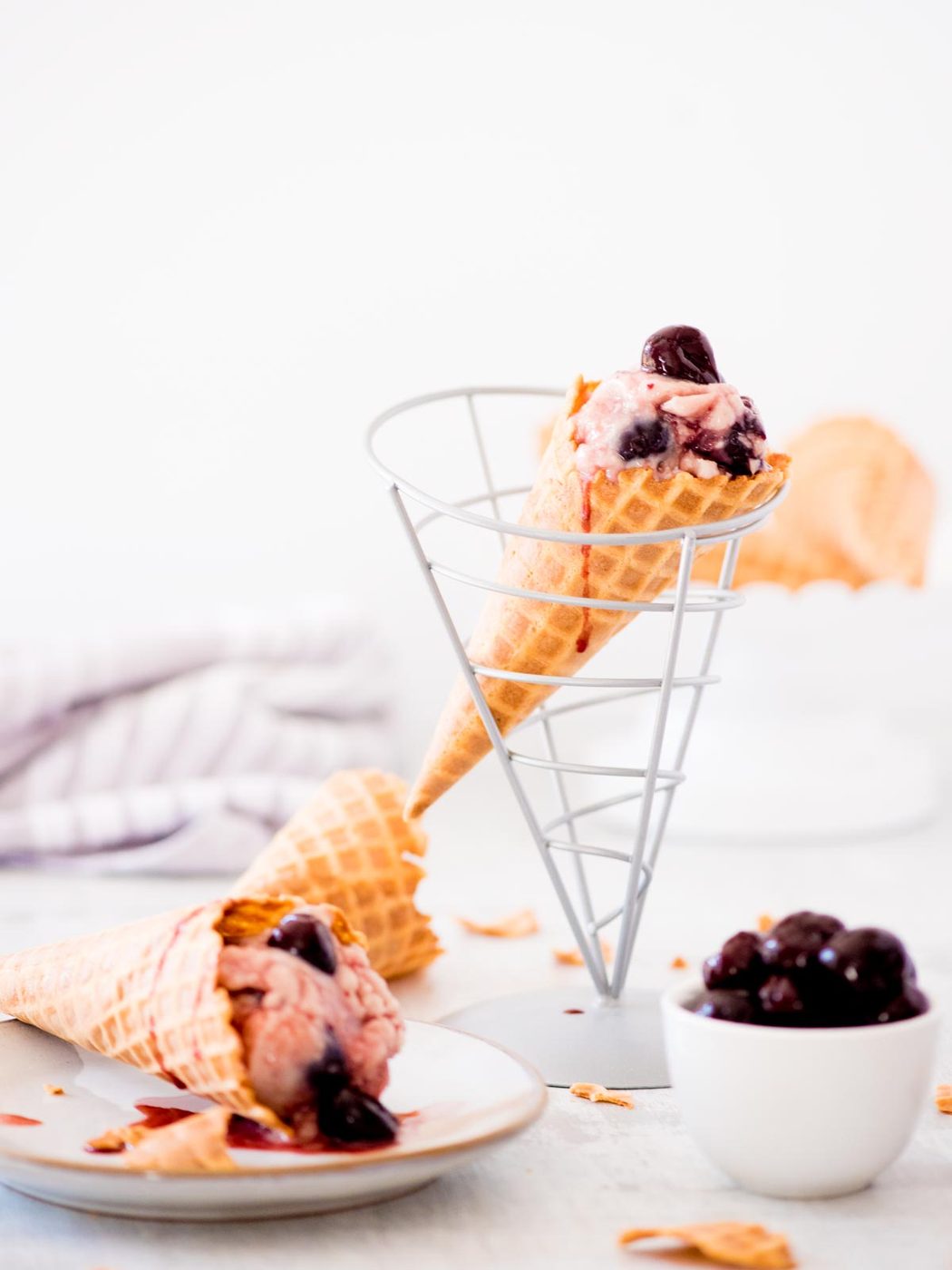 from-scratch dark cherry ice cream in a cone with a bowl of cherries and another cone on a plate