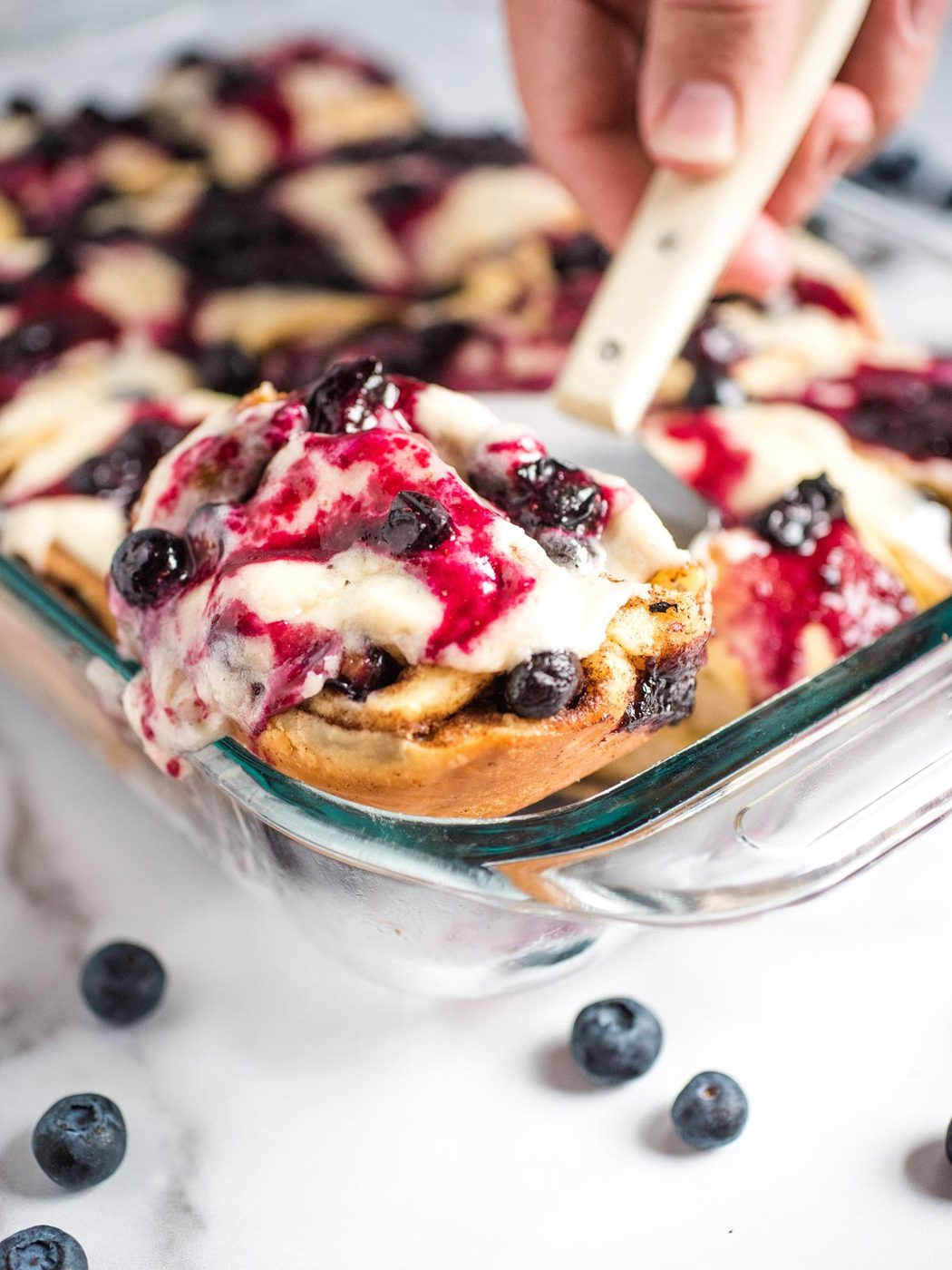 blueberry cinnamon roll being scooped out of baking dish with spatula