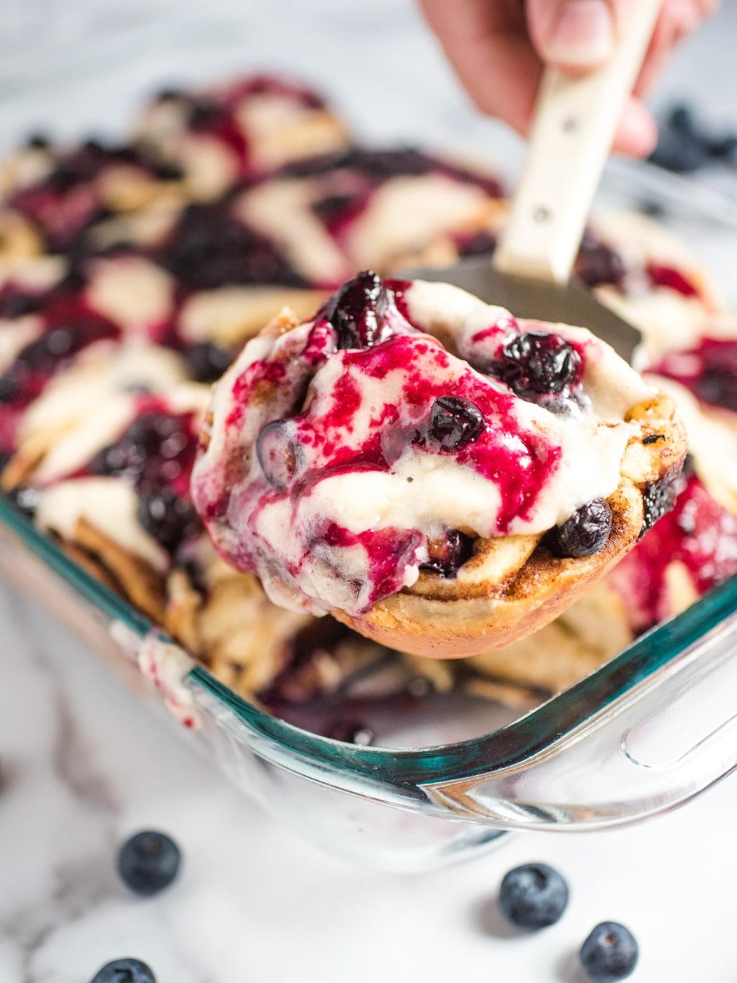 blueberry cinnamon rolls inside pyrex dish being scooped out with a spatula