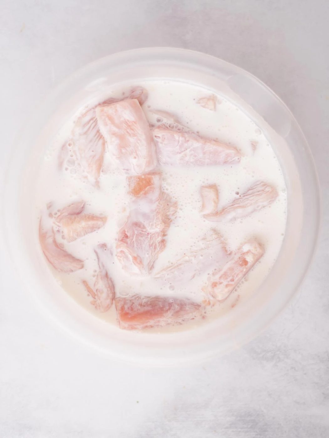 Raw chicken pieces and buttermilk combined in a mixing bowl.