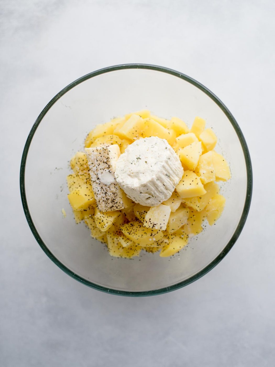 Cooked potatoes added to a bowl with seasonings and boursin cheese added to the top.