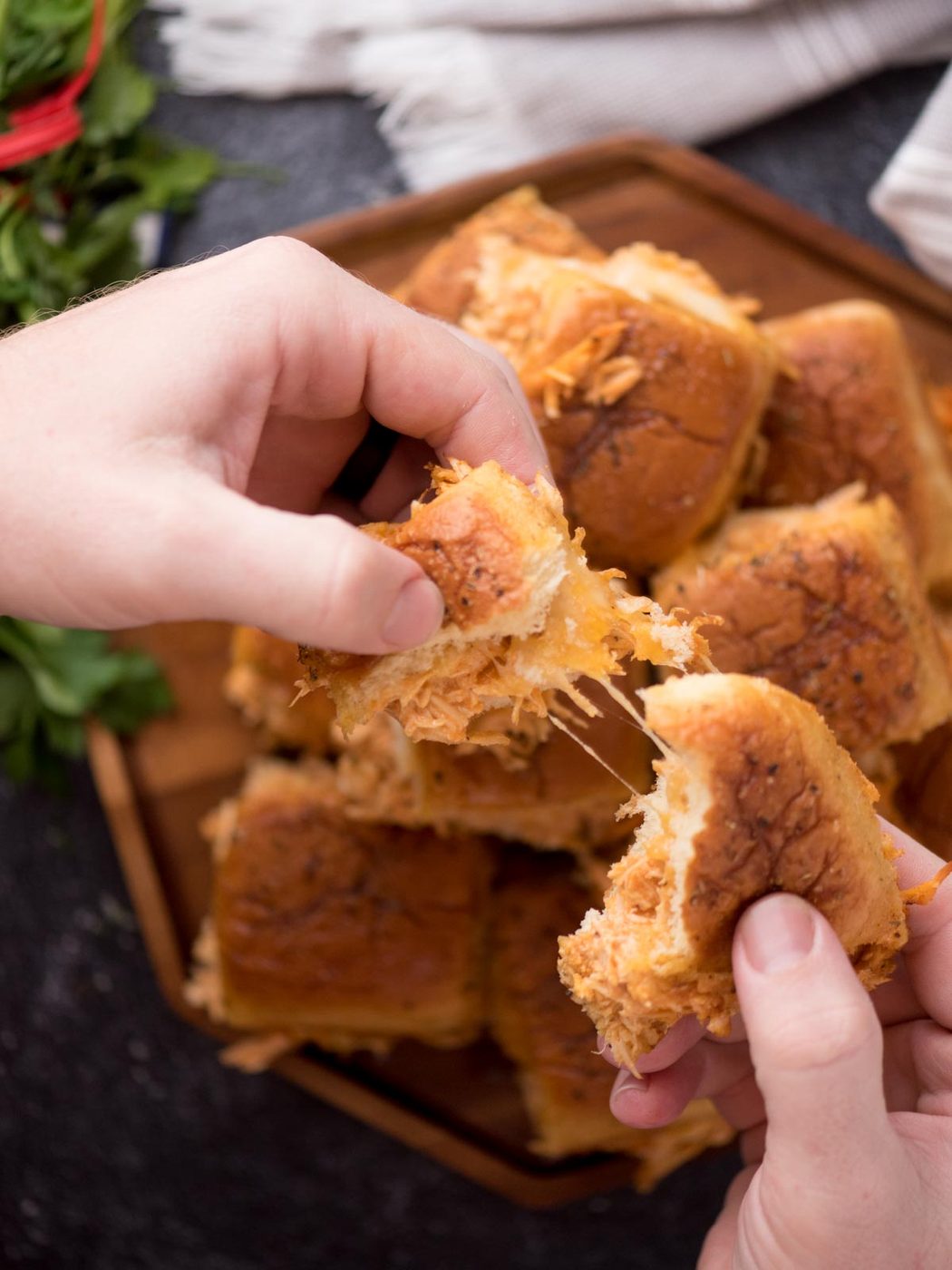 Hand pulling apart a cheesy buffalo chicken slider.