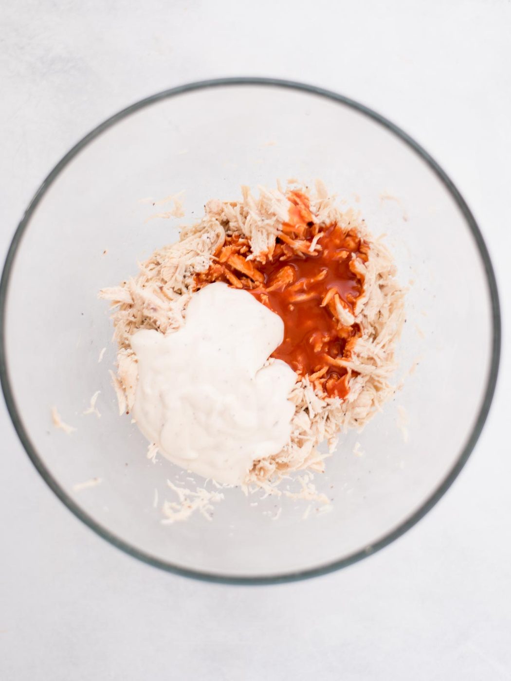 Shredded chicken in a bowl with seasonings measured out over top of it.