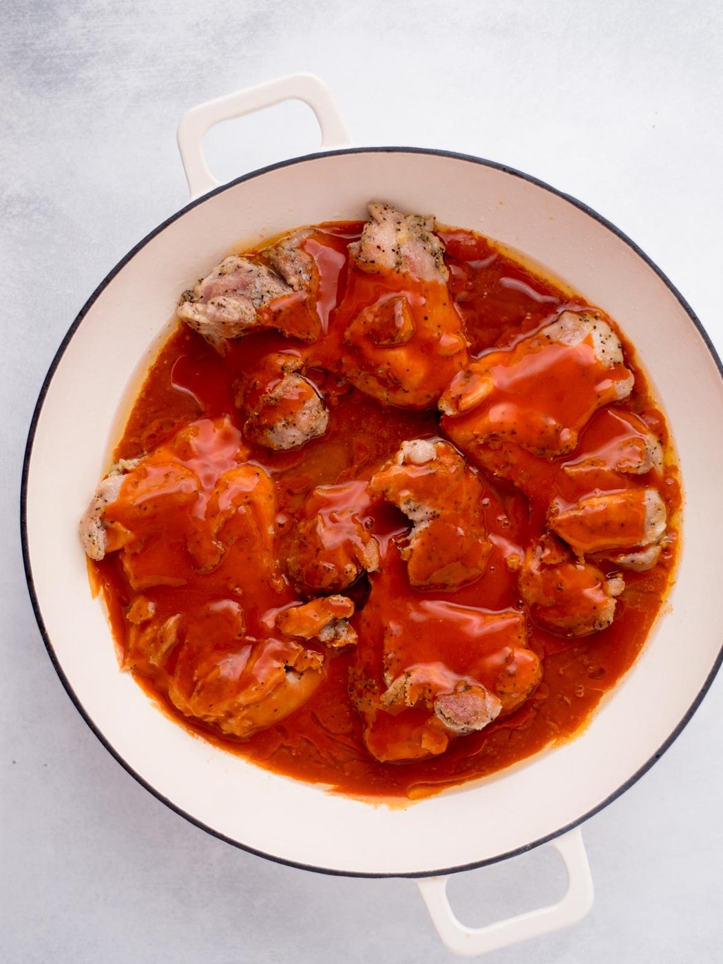chicken thighs seared in a skillet topped with buffalo sauce