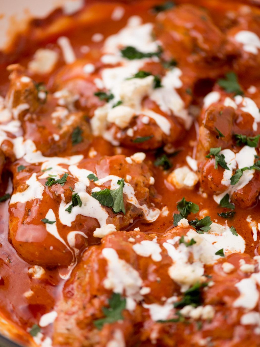 buffalo chicken thighs in a skillet surrounded by fresh parsley, a serving utensil, and a kitchen towel