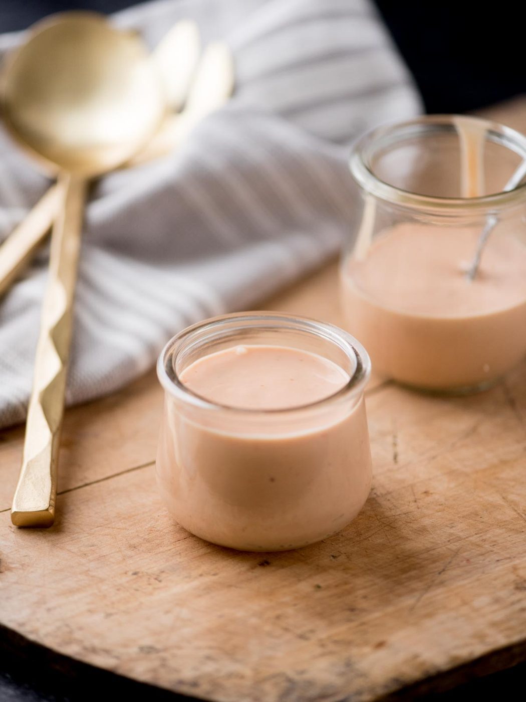 burger sauce in two glass jars on a bread board. It is surrounded by a kitchen towel and serving utensils