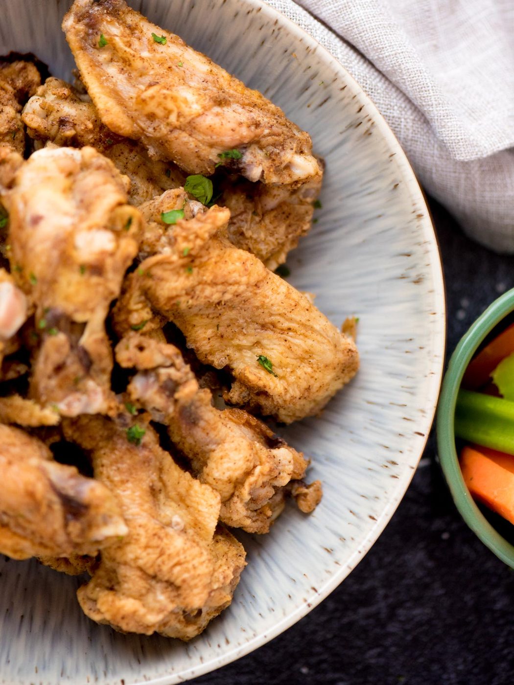 Partial view of cajun chicken wings with a small bowl of veggies alongside it.
